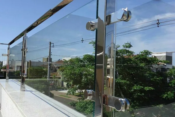 A glass balcony railing with a silver frame and a reflection of a house in the background.