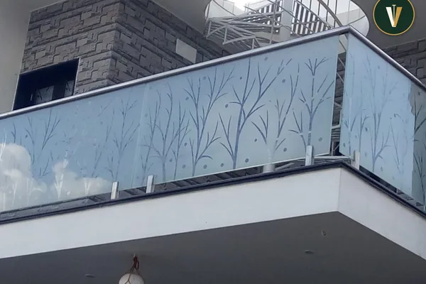 A framed glass balcony railing with a white frame and a design of trees on it.