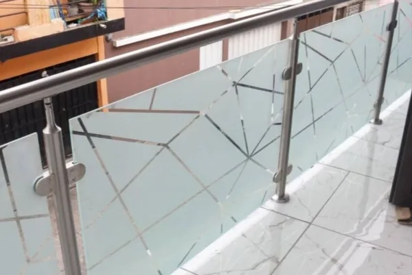 A balcony railing is shown in a close up shot with a glass door and a metal hand rail.